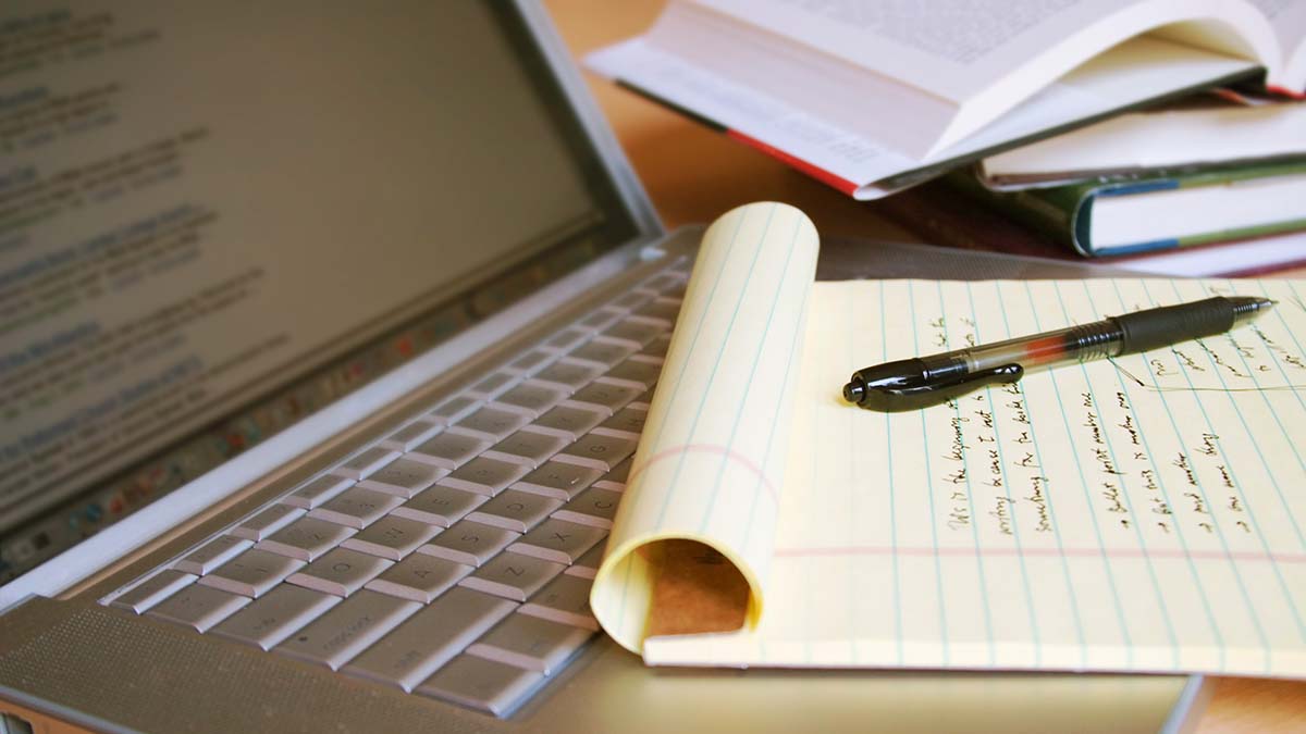 Apply | Laptop computer with books, pen and yellow legal pad