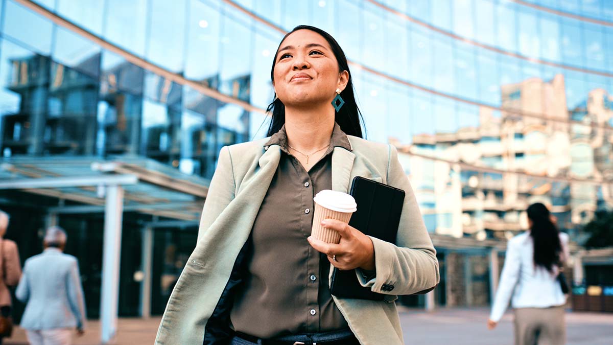 Fellows Recipients | Confident Businesswoman Walking with Coffee Outside Modern Office Building