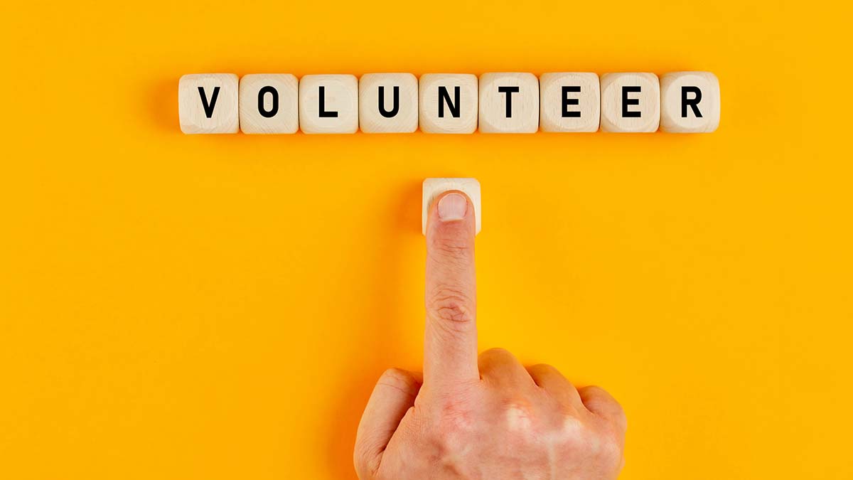 Volunteer Opportunities | The word volunteer written on wood blocks with a male hand pushing the button. Concept of volunteering and joining a cause.