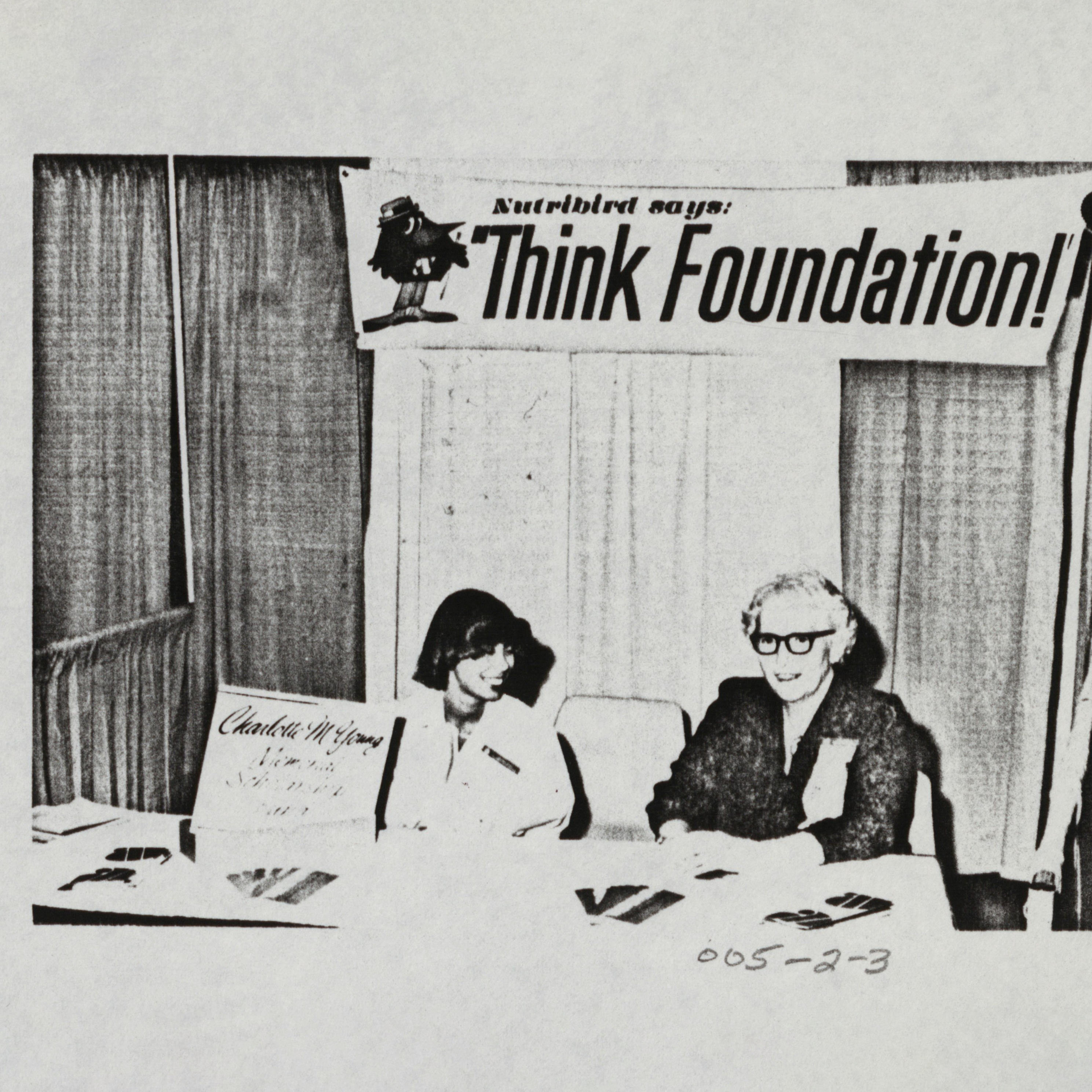 Two women sit at a booth with a "Think Foundation" sign